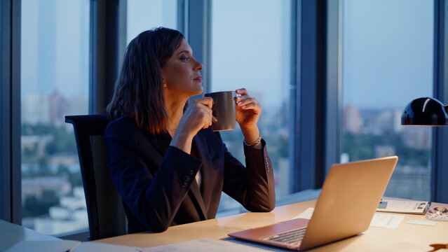 Relaxed entrepreneur drinking coffee at evening workplace closeup. Calm woman