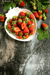 Fresh summer strawberries in white bowl on dark rustic surface. Top view flat lay background. Copy space.