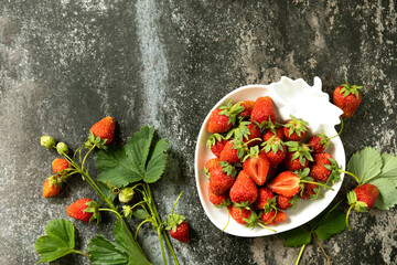 Fresh summer strawberries in white bowl on dark rustic surface.