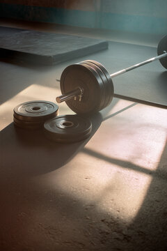 Weightlifting equipment in a gym with barbell and plates. A square of light illuminates the scene creating a strong, sporty feeling.