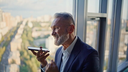 Aged entrepreneur talking speakerphone cellphone standing by window closeup.