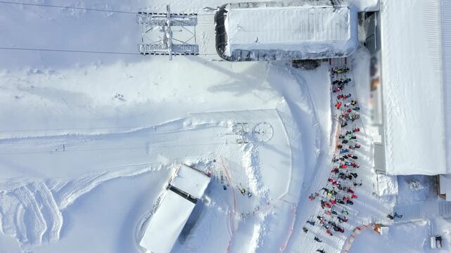 Aerial view of queue for ski lift at snowy winter resort. People in colorful gear waiting at the slope. Perfect for themes of skiing, tourism, winter sports, and mountain lifestyle.