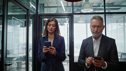 Successful businesspeople walking hallway looking cellphones closeup. Partners
