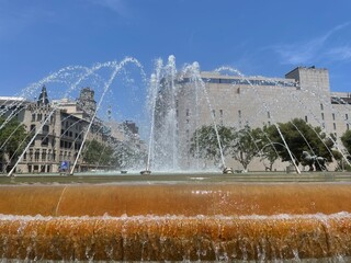 Beautiful view of a large fountain in Pla&ccedil;a de Catalunya, Barcelona, on a sunny day. Water jets create a graceful arc against the backdrop of historic and modern architecture.