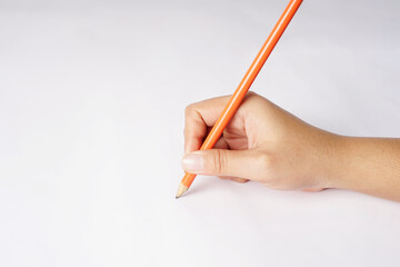 A hand clutching an orange-colored pencil in front of a white background