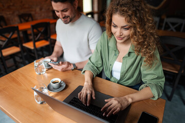 Fototapeta premium Young woman working on laptop while man using smartphone in cafe