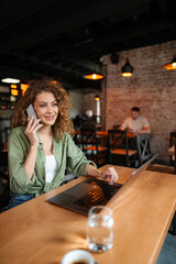 Young woman working on laptop and talking on phone in a cafe