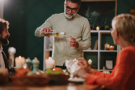 Senior man pouring white wine for family and friends during thanksgiving dinner