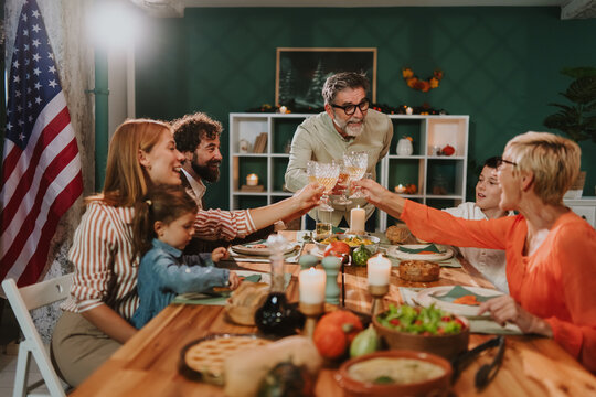 Family celebrating thanksgiving toasting with wine at home with american flag - Powered by Adobe