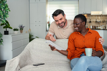 Fototapeta premium Happy multi-ethnic couple reading good news at home sitting on the sofa