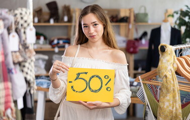 Happy young woman standing with banner announcing discount in clothing store