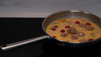 Frying pan with creamy sauce, sausage, and vegetables on stove