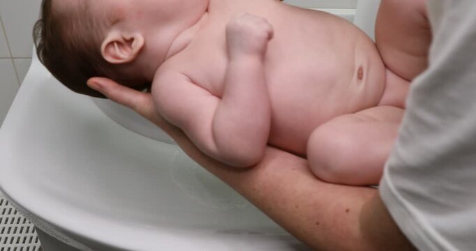 A baby girl washes herself in a bathroom sink