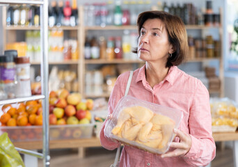 Female buyer carefully reads labels on packaging of semi-finished chicken products - she chooses best product in the supermarket
