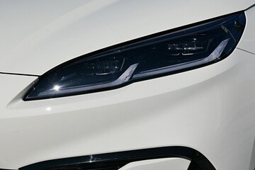 Detal of sleek elegant headlight of modern chinese hybrid electric sedan car, white color.