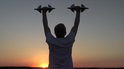 Sports are healthy lifestyle. Man exercising with dumbbells in park at sunset. Strong, mature man exercising outdoors. Man doing strength training, lifting dumbbells outdoors. Human, fitness outdoor