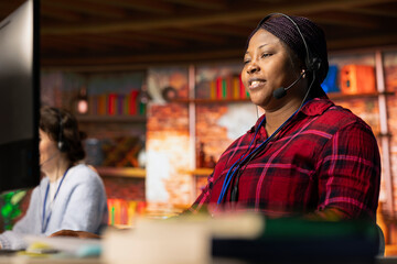 Smiling call center worker using headset microphone to answer customers technical inquiries about hardware issue. Happy woman doing customer support job using PC to troubleshoot problems