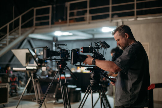 The director of photography with a camera on the set. A professional videographer is working on filming a movie or commercial for a TV series. The filming process takes place indoors in a studio.