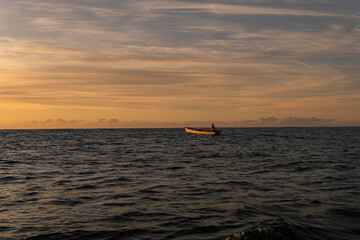Fototapeta premium Golden sunrise in Itacaré, Bahia, Brazil. Boats floating on calm sea, yellow light on the horizon, tropical coastal landscape with warm tones and natural beauty.