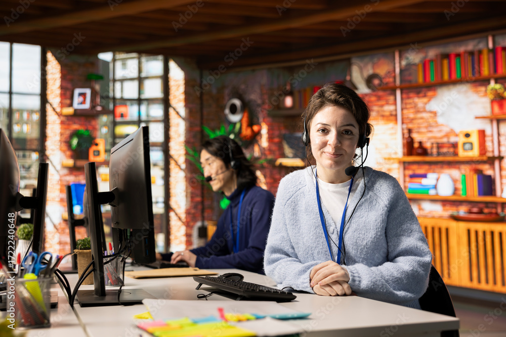 Poster portrait of smiling call center employee wearing headset resolving customers concerns, speaking into