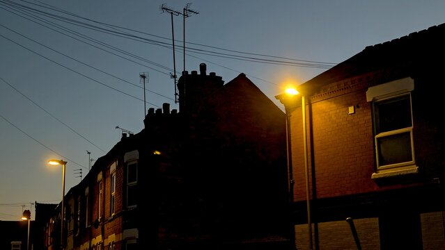 A row of British terraced houses silhouetted against a dark evening sky, with streetlights illuminating the scene, perfect for illustrating urban life or late-night commuting