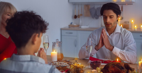 Big multi generation family praying at table before Christmas dinner at home. Children, their parents and grandmother praising God, saying prayer, thankful for Xmas holiday meal