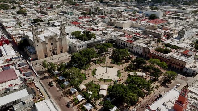 Aerial push in and crane down toward main square with colonial buildings and trees in historic center of Merida, Mexico