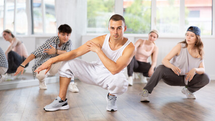Fototapeta premium Active young guy performing seated pose of breakdance in training hall during dancing classes