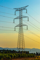 Silhouette of a black electricity transmission tower with power lines stretching across the sky at sunset. Vertical photo