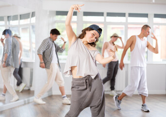 Fototapeta premium Advertising poster of dance training studio. Girl in loose sports clothes poses against background of dancing people, young guys. Hip hop dancing for young people, amateurs and professionals.