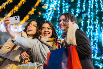 Three friends smiling and posing for a selfie while shopping at a festive christmas market
