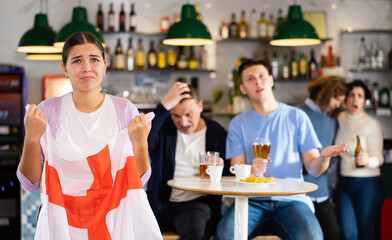 Company of young adult sports supporters with national flag of England upset about favorite team losing match in bar