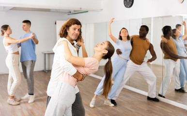 Fototapeta premium Woman and man practicing social dance moves in pair during group class