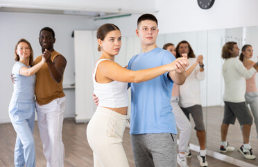 Fototapeta premium Smiling dancing people practicing movements while dancing in pairs in dance school for adults