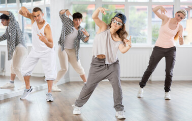 Fototapeta premium Young girl standing performs basic hip hop movements in front of group of students. Developing precise movements, rehearsing arc elements, nae nae moving