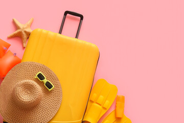 Suitcase with starfish, inflatable armbands, flippers and beach accessories on pink background © Pixel-Shot