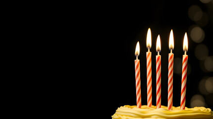 Burning birthday candles on a dark background cast a yellow glow of light over a celebration cake