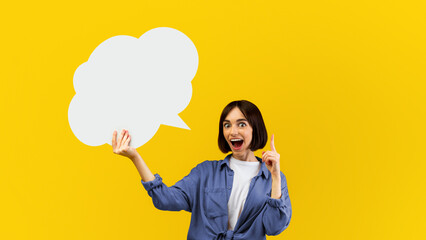 Wow idea concept. Surprised woman holding blank speech bubble and finger up, space with mockup for ad design over yellow studio background. Lady showing empty word box, free space