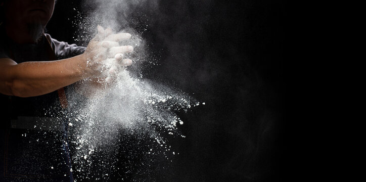 Chef prepare white flour dust for cooking bakery food. Elderly man Chef clap hand, white flour dust explode fly in air. Flour stop motion in air with freeze high speed shutter, black background