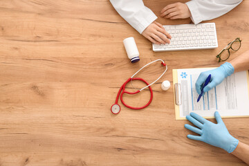 Doctor's hands with clipboard and computer keyboard near stethoscope on wooden table