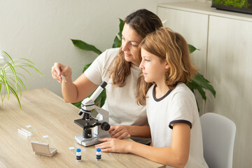 Mother and daughter explore science together using a microscope during online learning at home