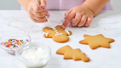 Child's hands decorating gingerbread man cookie with white icing, enjoying christmas holiday baking, creating festive treats with sprinkles, celebrating winter season traditions