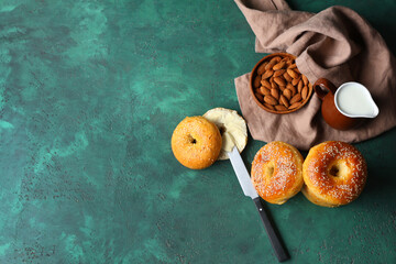 Tasty bagels with almond nuts and jug of milk on green background