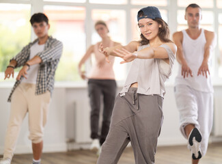 Naklejka premium Young girl standing performs basic hip hop movements in front of group of students. Developing precise movements, rehearsing arc elements, nae nae moving