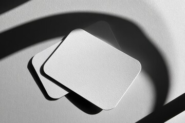 Two blank, rectangular pieces of textured white paper, overlapping, set against a light gray background with dramatic shadows