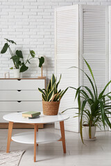 Table with books and houseplants near white brick wall in interior of living room