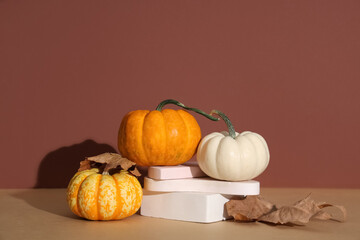 Decorative podiums with fresh pumpkins and autumn leaves on brown background