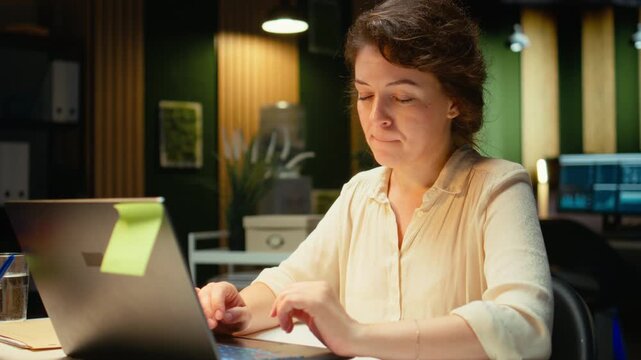 Female manager engaged in writing notes for a presentation on her laptop, extracting essential highlights from finance documents and making a summary for business goals and upcoming tasks. Camera A.