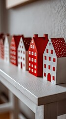 A row of small, painted wooden houses in red and white sits atop a light gray wooden shelf.
