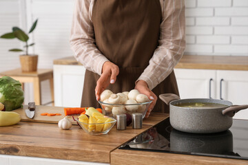 Young woman with fresh vegetables cooking soup in kitchen, closeup
